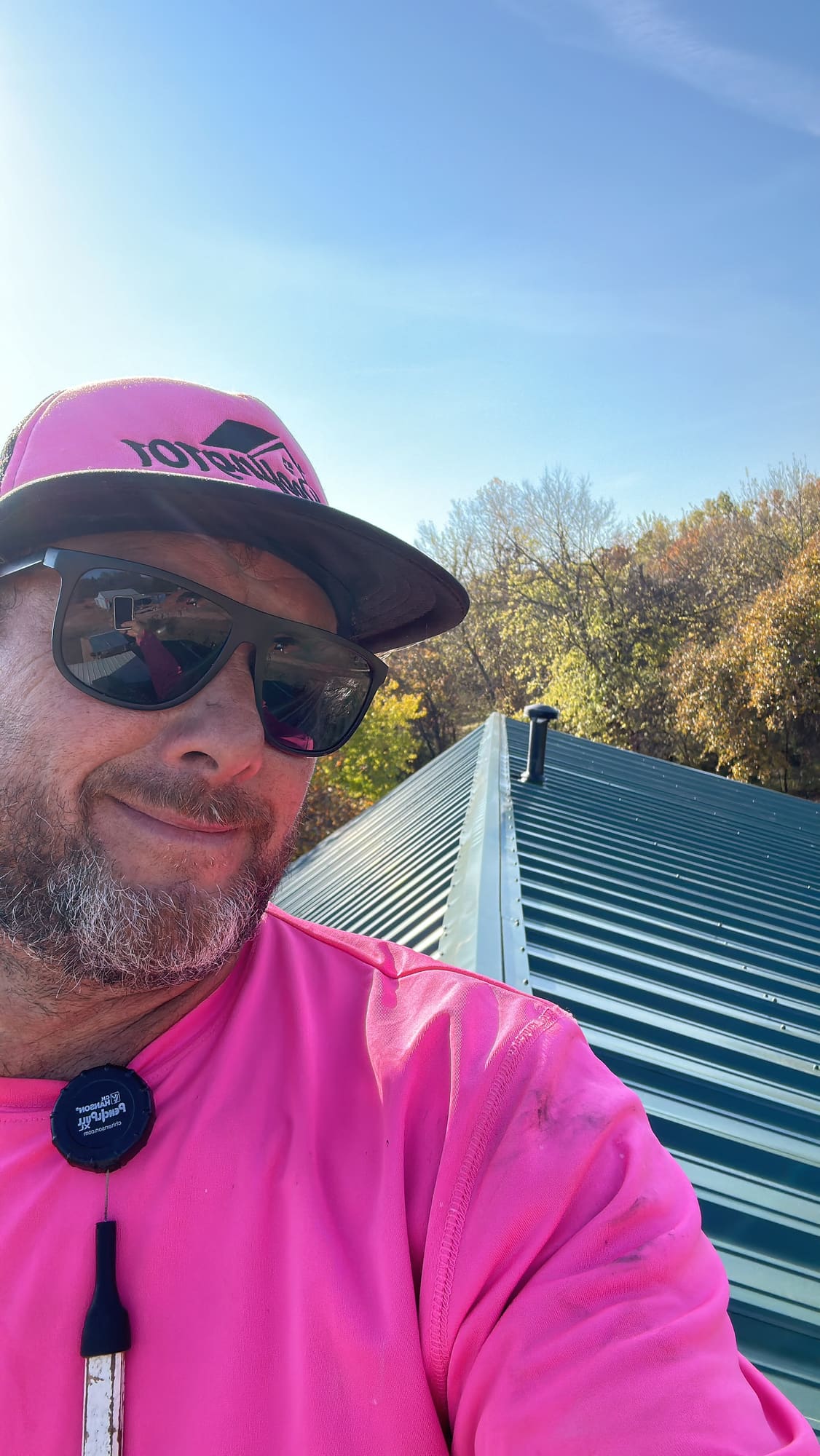 Matt Taylor, owner of Roofing 101, on a metal roof in his pink Roofing 101 hat and shirt